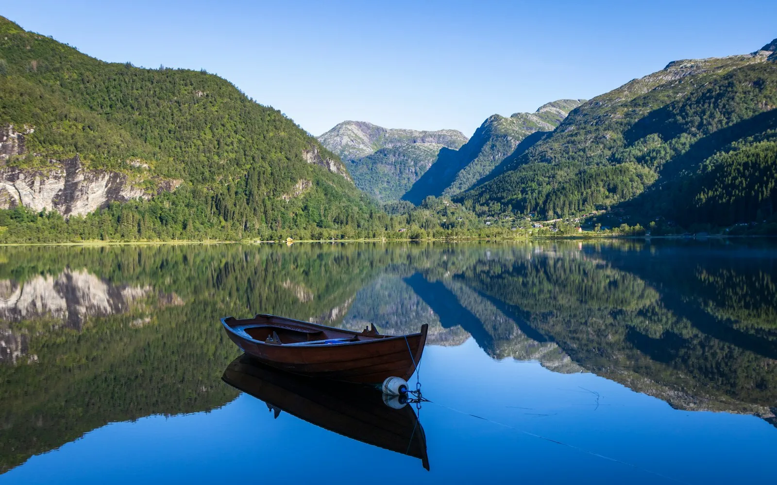 A wooden rowboat moored on a mirror-still lake, with green mountains reflected in the water
