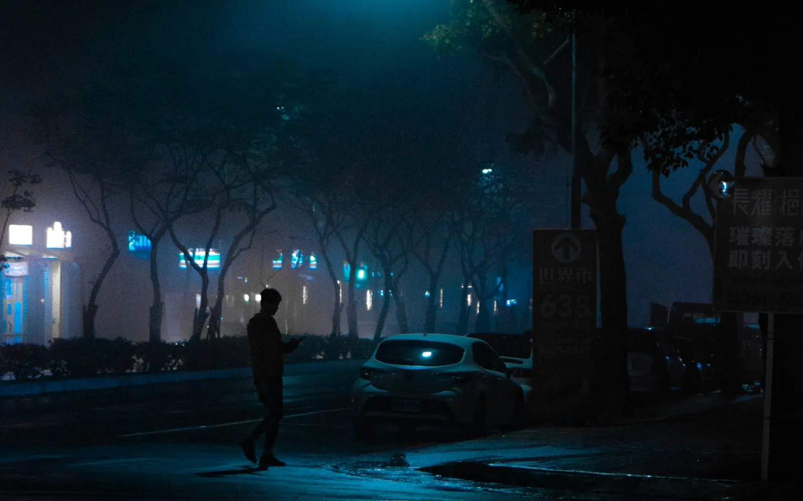 A lone figure crossing a misty street under a streetlight at night