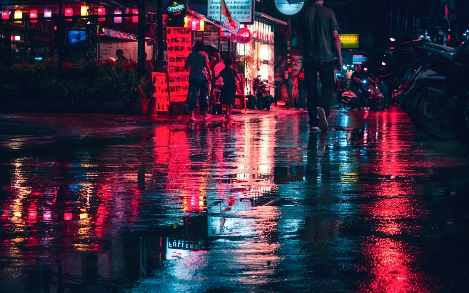 Neon signs and red lights reflected on a wet street at night