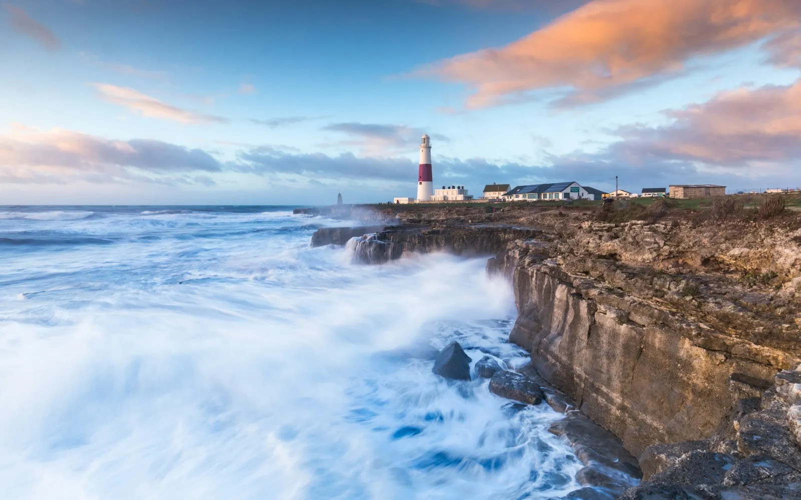 A red and white lighthouse on a limestone headland as surf pours over the rocky cliffs below
