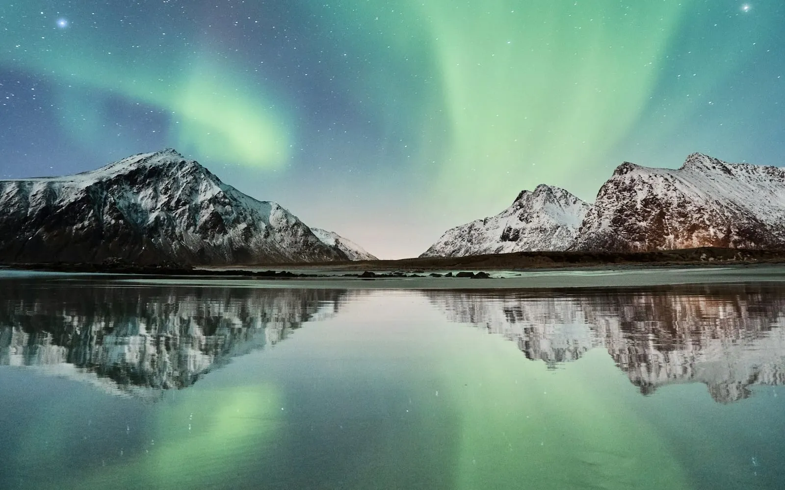 Northern lights above snowy mountains, reflected in still water